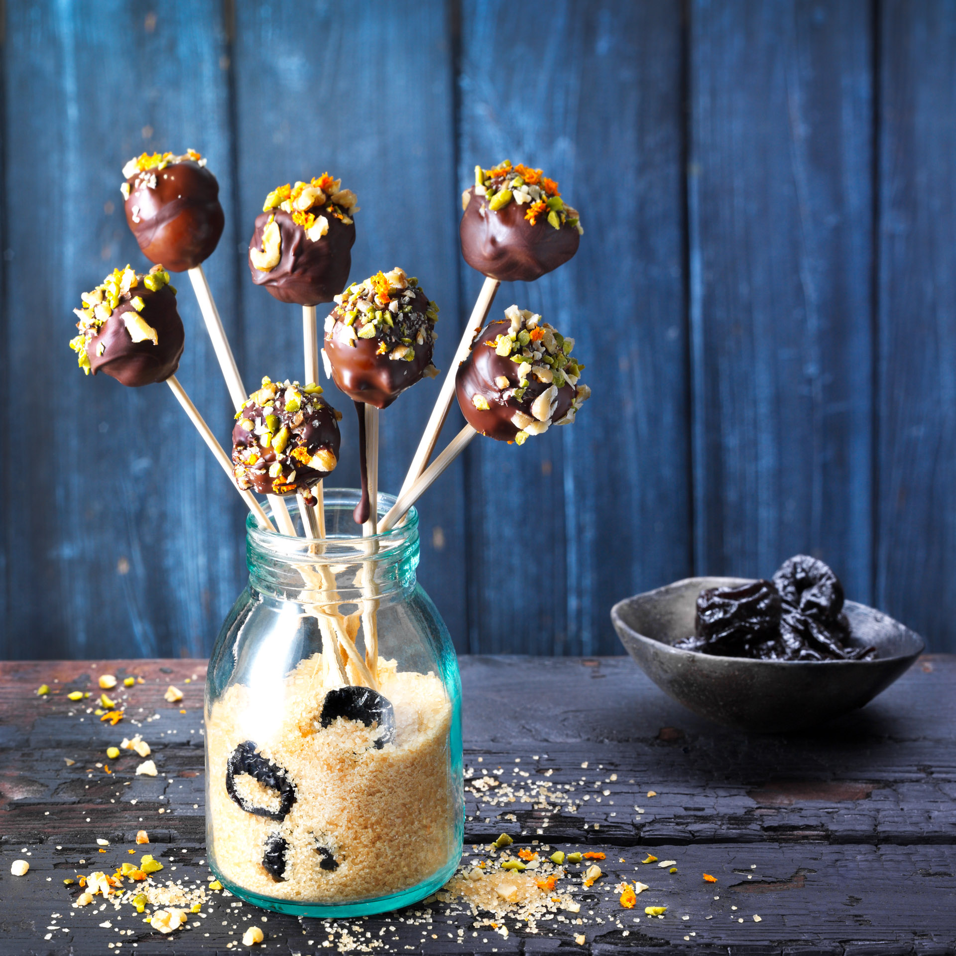 Marzipan, orange, and a trio of nuts form the filling for these prune and and chocolate lollipops. For coating the lollipops, source couverture chocolate, which has a higher percentage of cocoa butter and is ideal for tempering and dipping.
